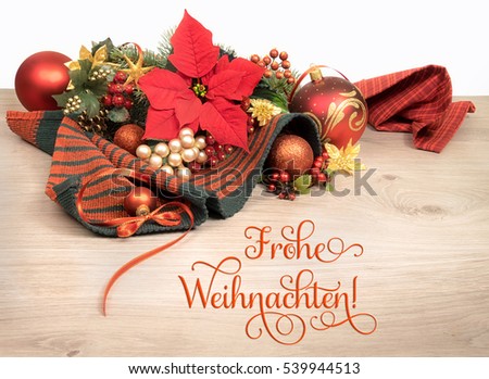 Wooden background with poinsettia and decorated Christmas tree twigs, text on the picture means "Merry Christmas" in German. 