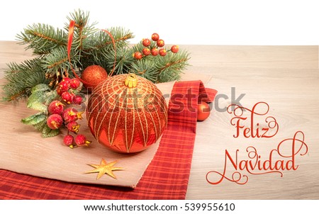 Wooden background with decorated Christmas tree twigs, text on the picture means "Merry Christmas" in Spanish