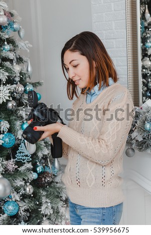 Photographer woman making a photo shoot with professional photocamera in the new year interior with decorated Christmas tree