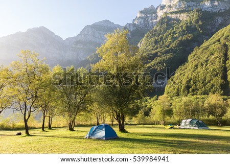 Two tourist tents in the forest  against majestic mountains, lit by the morning sun. Alps. Switzerland.