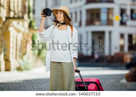 Outdoor summer smiling lifestyle portrait of pretty young woman having fun in the city in Europe with camera travel photo of photographer Making pictures in hipster style glasses and hat
