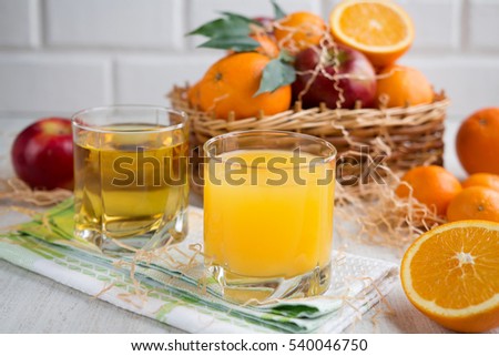Fresh orange and apple juice in a glass on a background of fruit baskets