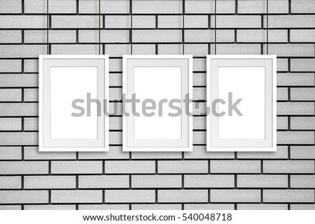 Three frames hanging on cords against  white bricks wall, gallery style decor mock up