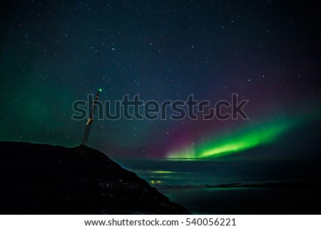 Radio tower on the hill and northern lights over the fjord in the background