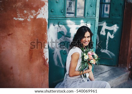 young and happy girl with a bouquet sits near green doors
