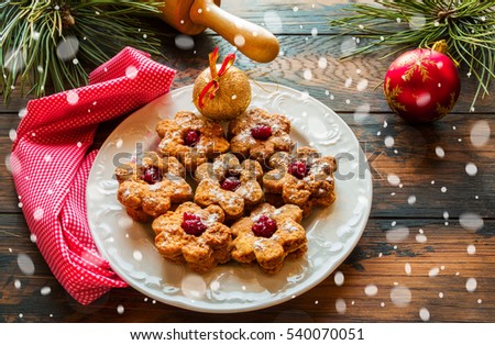 Christmas Linzer homemade cookies with strawberry jam on wooden background. White plate, festive decoration, snow effect.