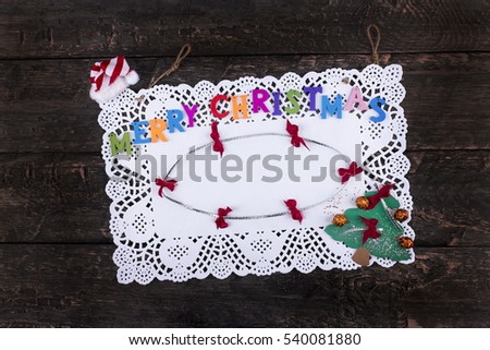Merry Christmas greeting text written with small, colorful, wooden letters on a pure white napkin, placed on a wooden, vintage look background- Top view