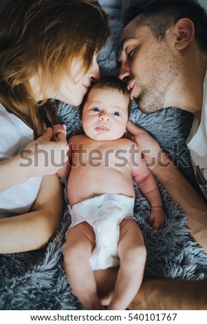 Happy family. Young parents lying in bed kissing cute small newborn baby. Closeup portrait.