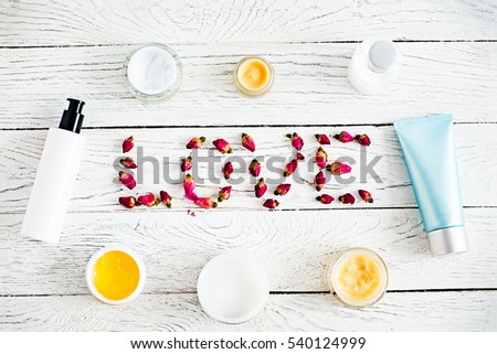 Word Love with rose buds and various cosmetics jars and tubes, branding mock-up for body and skin care creams on a whitewash wooden background. Placing  own design. Top view. Organic beauty products.