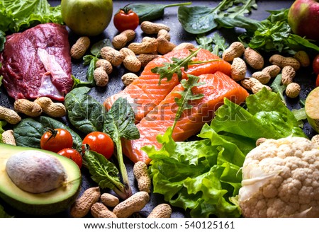 Fresh fish, meat, vegetables, fruits, nuts on black chalk board background. Cauliflower, avocado, apples, tomatoes, salmon, beef, spinach, herbs. Diet/healthy/paleo food. Ingredients for cooking Royalty-Free Stock Photo #540125161