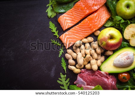 Fresh vegetables, fruits, fish, meat, nuts on black chalk board background. Cauliflower, avocado, apples, tomatoes, salmon, beef, spinach, herbs. Diet/healthy/paleo food. Ingredients. Space for text Royalty-Free Stock Photo #540125203