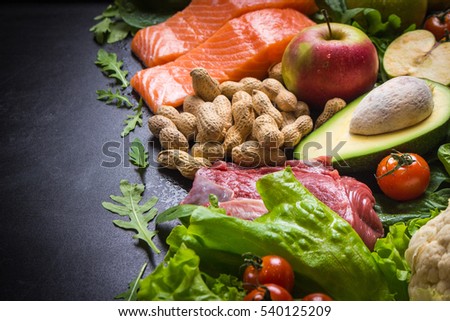 Fresh vegetables, fruits, fish, meat, nuts on black chalk board background. Cauliflower, avocado, apples, tomatoes, salmon, beef, spinach, herbs. Diet/healthy/paleo food. Ingredients. Space for text