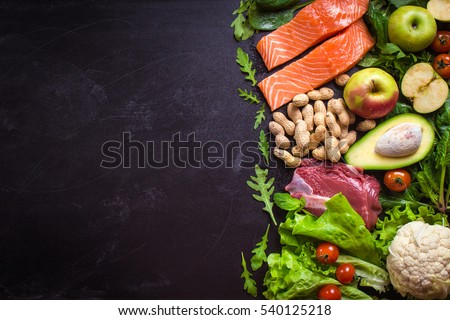 Fresh vegetables, fruits, fish, meat, nuts on black chalk board background. Cauliflower, avocado, apples, tomatoes, salmon, beef, spinach, herbs. Diet/healthy/paleo food. Ingredients. Space for text Royalty-Free Stock Photo #540125218