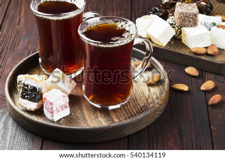 Black tea, oriental sweets, dates and nuts on a dark wooden background.