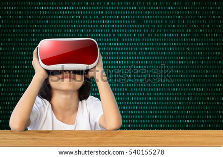 Child with virtual reality goggles sitting behind green background.