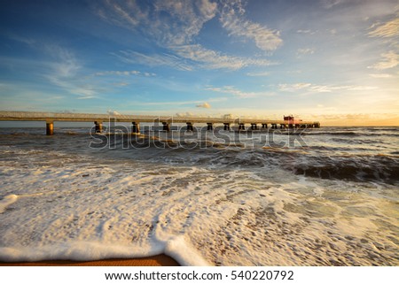 Beautiful scenery of sunset sky at beach with wave motion at foreground and long jetty at background. Motion blur on the foreground due to slow or fast shutter speed shot. Composition of nature.