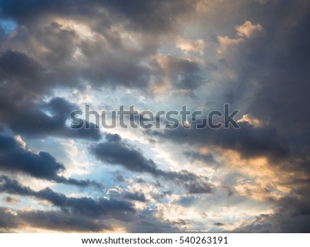 Picture of the sunset cloudy sky reflecting orange sun rays. Background of the still blue sunset sky with sun rays reflecting from the clouds.