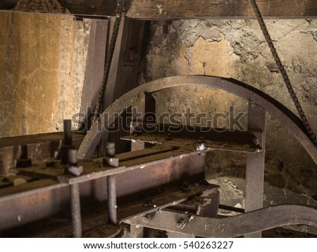 Picture of the rusty mechanism in the wooden belfry of the church. Rusty mechanism for church bell against the old yellow wall of the belfry.