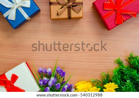 Four gift boxes in blue, brown,red and pearl white color with ribbon and plastic flowers above wooden texture background table with copy space