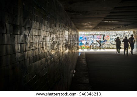 tunnel underground crossing with silhouette of three pedestrian  with pictures of graffiti on the walls. The original light-shadow gradation. Ideal for the creative design of stage. Selective focus.