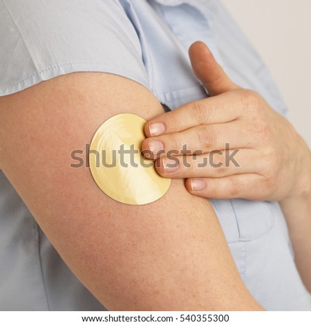 ATTRACTIVE HEALTHY YOUNG BLONDE WOMAN APPLYING FLESH COLOURED NICOTINE PATCH TO ARM Royalty-Free Stock Photo #540355300