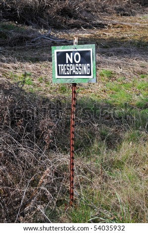 No trespassing sign post stuck in a grass field
