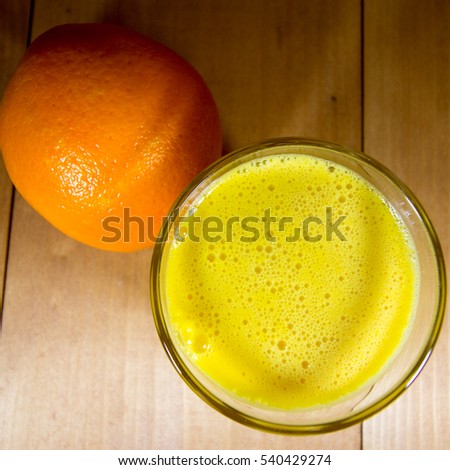 Freshly squeezed orange juice and whole orange on walnut wood table surface.