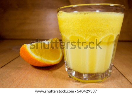 Fresh orange juice in transparent glass with piece of orange on walnut wood surface.