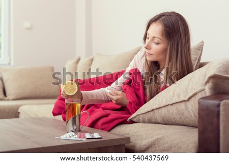 Sick woman lying in bed with high fever and a flu, squeezing a lemon juice in her tea.