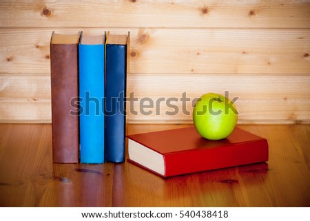 Books and green apple on wooden table over wooden background