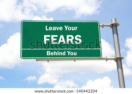 Green overhead road sign with a Leave Your Fears Behind You concept against a partly cloudy sky background.