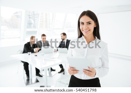 Business woman standing in office with business group on background and holding documents