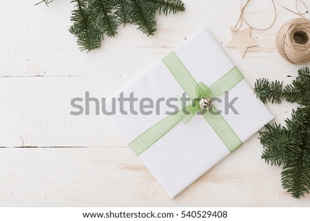 Christmas gift box with decorations. New Year present in white box with fir branches at white wooden table. Flat lay with copy space. Celebration, holiday season and winter concept