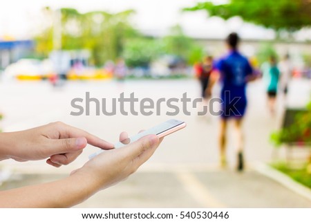 Man use mobile phone, blur image of people exercising in the park.