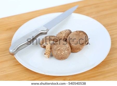 Shiitake mushroom with knife on white plate against wood background
