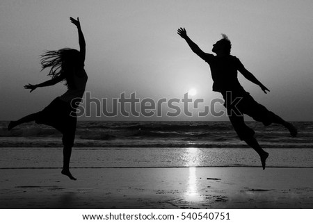 Silhouettes of happy couple jumping on background of sea at sunset