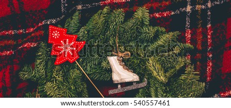 Pair of toy ice skates for figure skating and wooden christmas tree on a evergreen wreath and scottish tartan as a background. Winter holiday banner with copy space for text, wide panorama format.