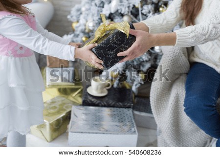 Mother and daughter opening christmas presents. Christmas tree on a background. Happy family holidays concept
