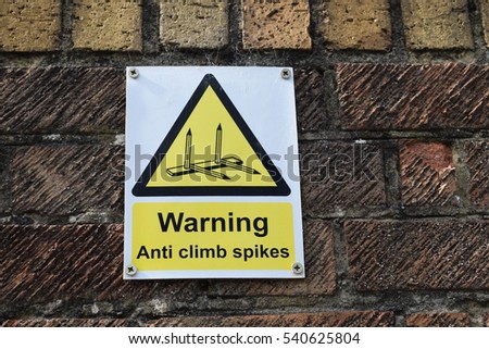 Dirty brick wall with a yellow and white warning sign in Tottenham