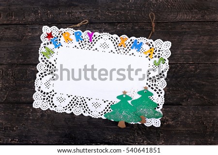 Merry Xmas greeting text written with small, colorful, wooden letters on a pure white napkin, placed on a wooden, dark, vintage look background- Top view