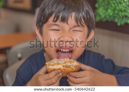 image of happy asian boy eating hamburger in restaurant .