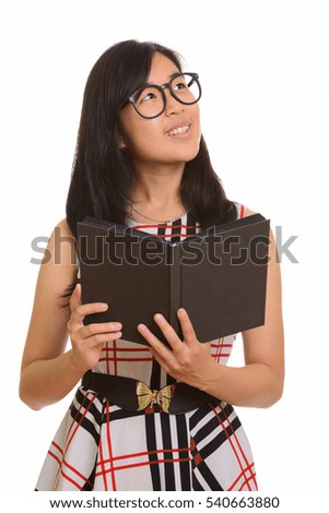 Young happy Asian businesswoman smiling and holding book while thinking isolated against white background