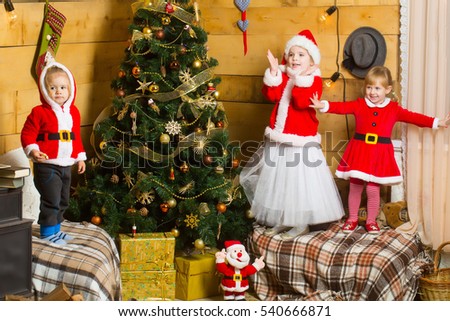 christmas happy children in red santa claus hat and coat play at xmas decorated tree. cute kids at new year holidays celebration on wood background