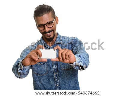 Young happy Indian man smiling and taking picture with mobile phone isolated against white background