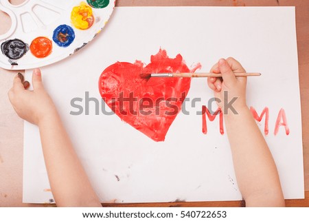 view from above. child draws a brush and paints on white paper. red heart