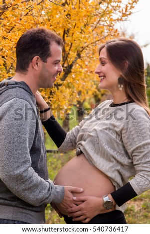 husband and pregnant wife in nature next to a yellow tree.