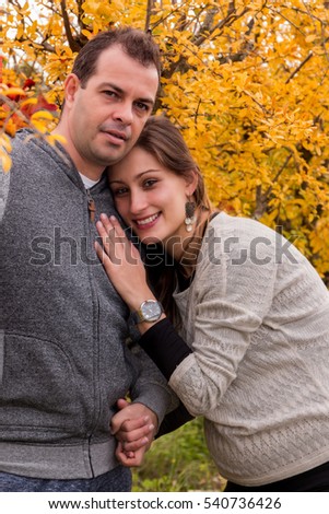 husband and pregnant wife in nature next to a yellow tree.