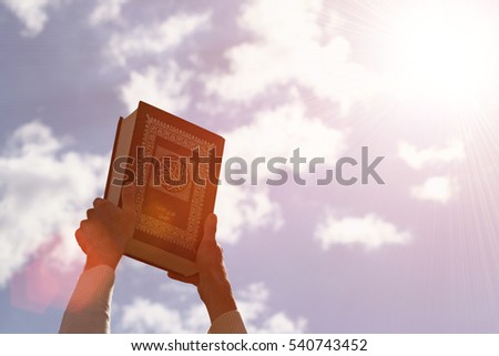 Man's hands holds Koran - holy book of muslims, on blue sky with clouds. With instagram style filter Royalty-Free Stock Photo #540743452