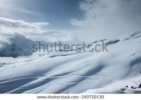 Ski in Elbrus region. A wide ski slope with a view of snow-covered Caucasus mountains. Clear Sunny day, blue sky and white clouds. Russia