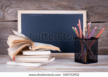 Stack of books, chalk blackboard with pencils on the wooden table